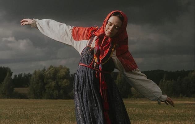Девушка в народном костюме танцует в поле